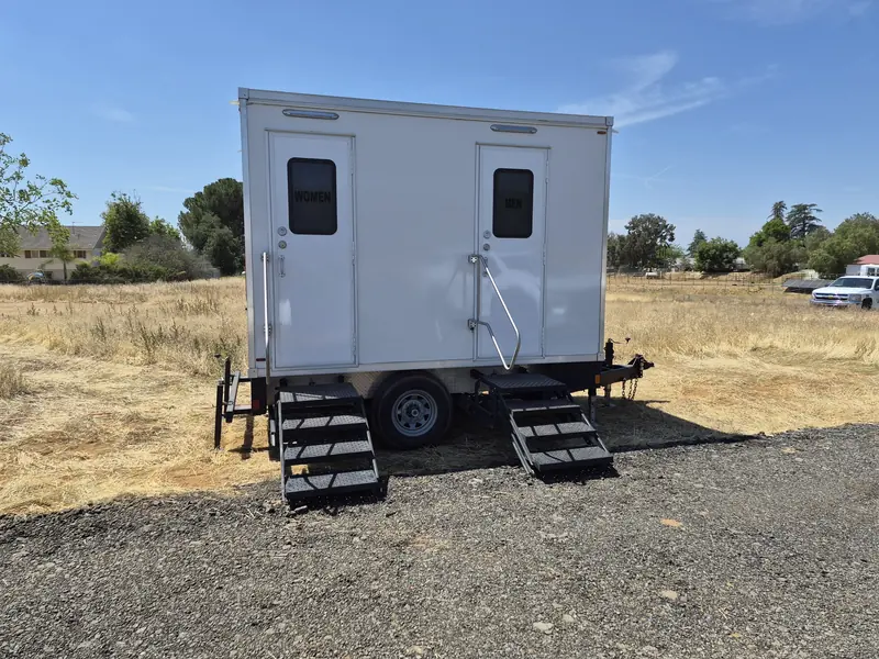 Restroom trailer on a gravel ranch pad with fields behind it